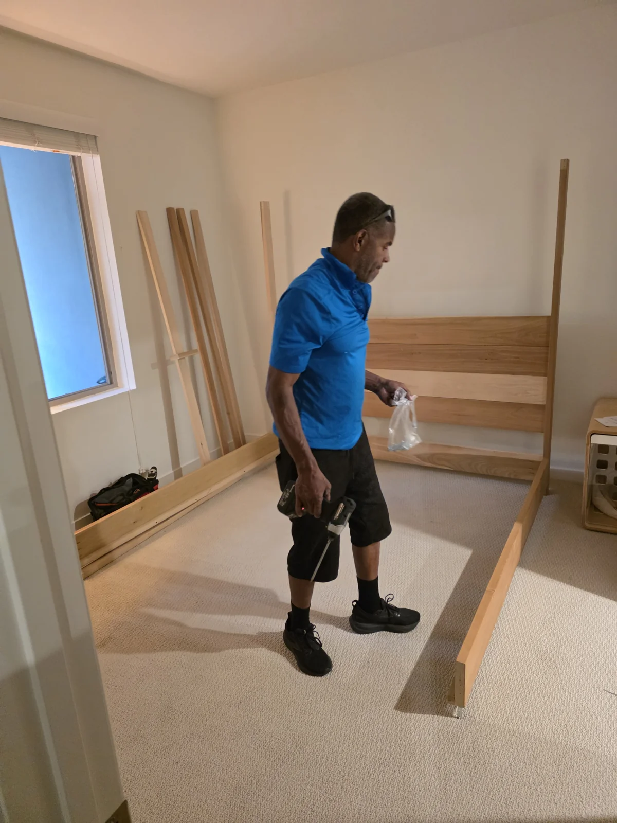 A mover in a blue uniform working with a wooden bed frame.