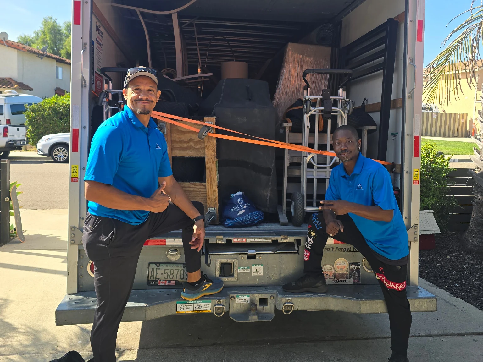 Two Soco Moves crew members in blue uniforms beside a loaded moving truck.