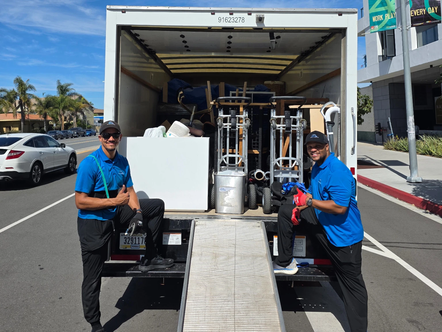 Two smiling Soco Moves crew members in blue uniforms beside a loaded moving truck.