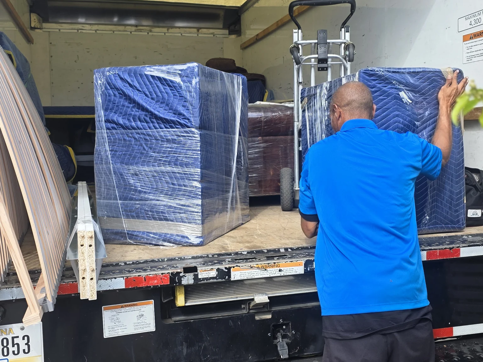 A mover in a blue uniform handling blanket-wrapped furniture at a truck.